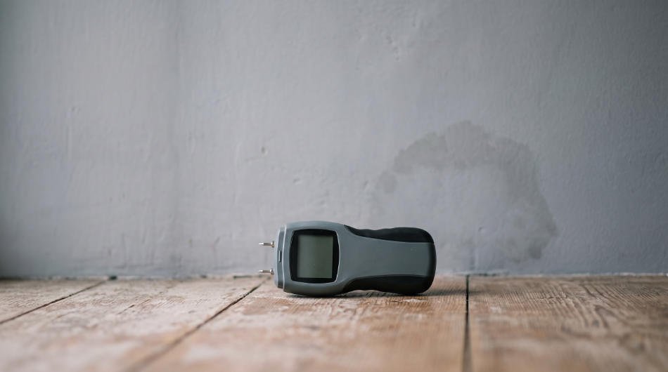 KI-generierter Platzhalter: Feuchtemessgerät auf einem Holzdielenboden vor einer Wand mit Feuchtefleck